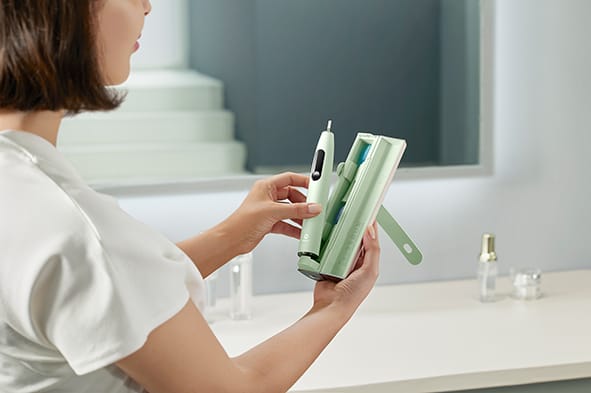 A woman places a green model of the toothbrush into its case.