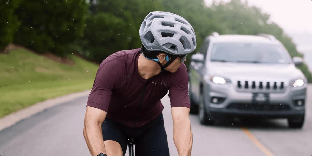 Cyclist checks a car over his shoulder. You can see he's wearing Shokz headphones.