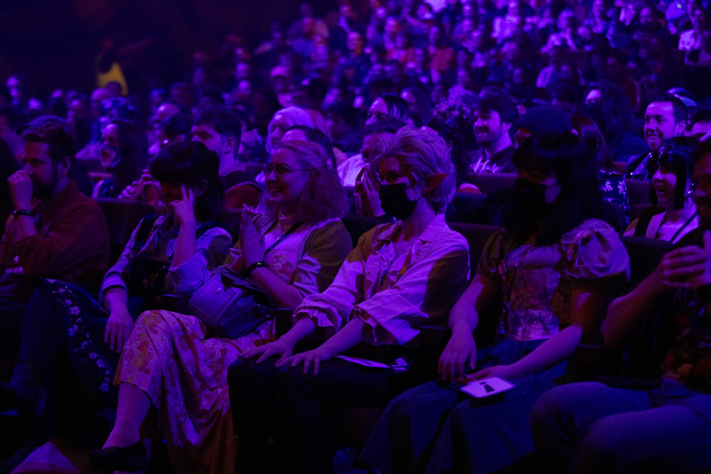 Photo of a crowd in a large theatre, seated in a blue lit darkened room.